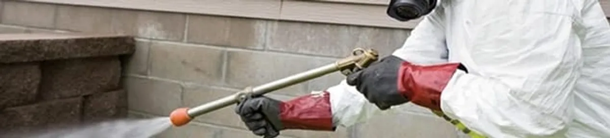 Pest control technician applying exterior insect treatment along a home foundation in Kansas City, MO