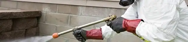 Pest control technician applying exterior insect treatment along a home foundation in Kansas City, MO