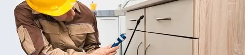 Roach exterminator applying treatment under kitchen cabinets in Kansas City, MO