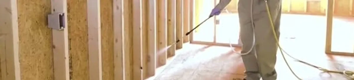Termite treatment technician applying spray along framing and unfinished walls in Kansas City, MO