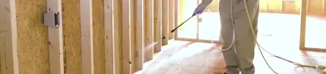 Termite treatment technician applying spray along framing and unfinished walls in Kansas City, MO