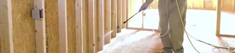 Termite treatment technician applying spray along framing and unfinished walls in Kansas City, MO